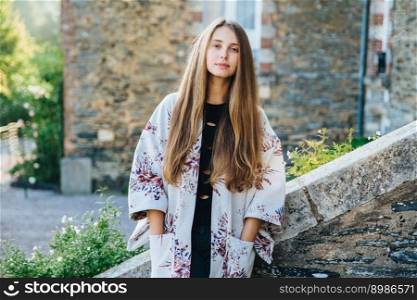 Confident pleasant looking young female poses against ancient bilduings as goes sightseeing in old town, wears fashionable clothes, poses outdoors. Female tourist admires beauty of city landscapes