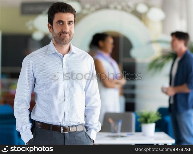 Confident professional standing in an offfice with colllegues on background