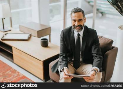 Confident senior businessman with digital tablet sitting in modern office