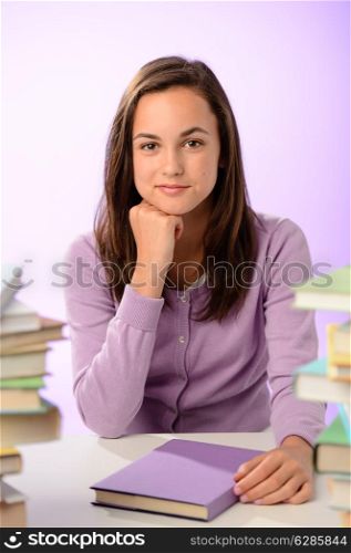 Confident student girl between stacks of books on purple background
