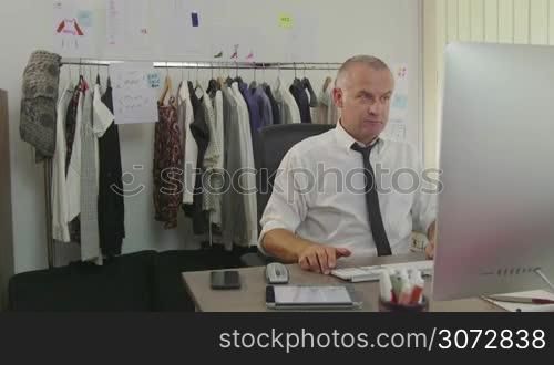 Confident, successful businessman, man working as fashion designer, manager with computer in studio, talking on mobile phone. People at work, career, success, business, industry, busy worker in office