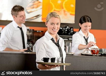 Confident waitress serving coffee with tray colleagues working behind