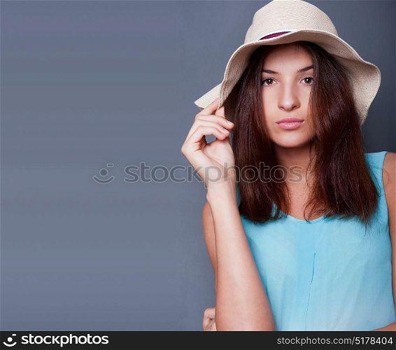 Confident woman with arms near her head holding hat against a blue background. Lots of copyspace. Square shot