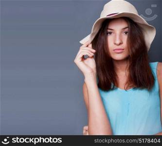 Confident woman with arms near her head holding hat against a blue background. Lots of copyspace. Square shot