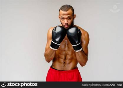 Confident young African boxer in boxing gloves standing over light grey background.. Confident young African boxer in boxing gloves standing over light grey background