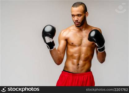 Confident young African boxer in boxing gloves standing over light grey background.. Confident young African boxer in boxing gloves standing over light grey background