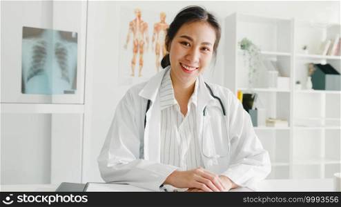 Confident young Asia female doctor in white medical uniform with stethoscope looking at camera and smiling while video conference call with patient in health hospital. Consulting and therapy concept.