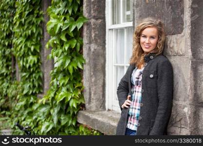 Confident young blond woman smiling an leaning against stone wall