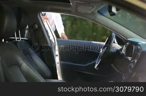 Confident young businessman getting into car, fastening seat belt before driving car. Serious handsome man in formal wear fastening safety belt and starting his vehicle&acute;s engine before going on business trip.