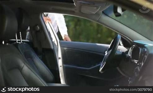 Confident young businessman getting into car, fastening seat belt before driving car. Serious handsome man in formal wear fastening safety belt and starting his vehicle&acute;s engine before going on business trip.