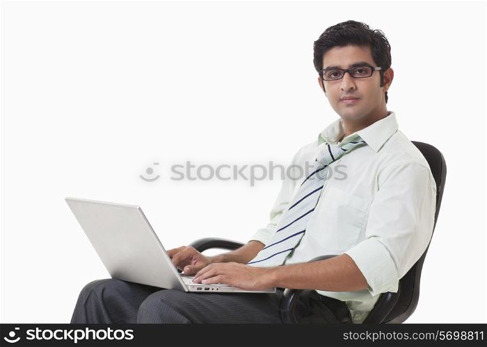 Confident young businessman on chair using laptop