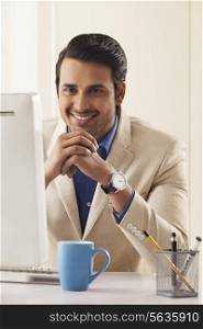 Confident young businessman smiling at computer desk