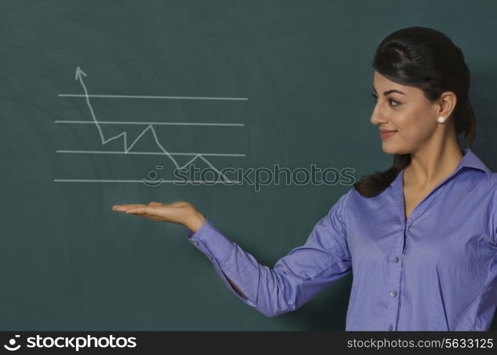 Confident young businesswoman displaying graph on green board at office