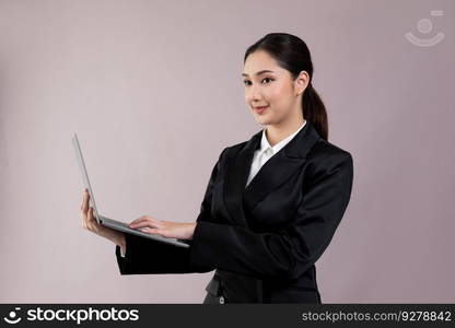 Confident young businesswoman stands on isolated background, working on laptop posing in formal black suit. Office lady or manager with smart and professional appearance. Enthusiastic. Businesswoman with laptop stands on isolated background. Enthusiastic