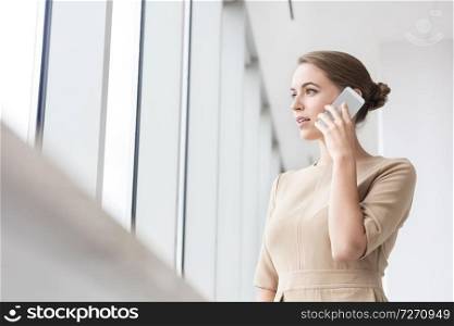 Confident young businesswoman talking on smartphone while standing at new office