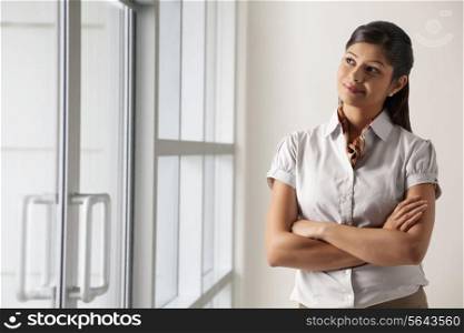 Confident young businesswoman thinking with arms crossed at office
