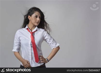 Confident young fashionable businesswoman with hand on hip standing against gray background