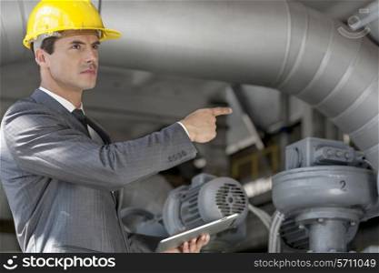 Confident young male manager with digital tablet pointing at machinery in industry