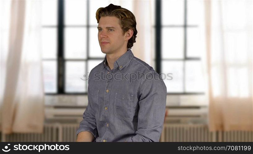 Confident young man in grey shirt by bright windows