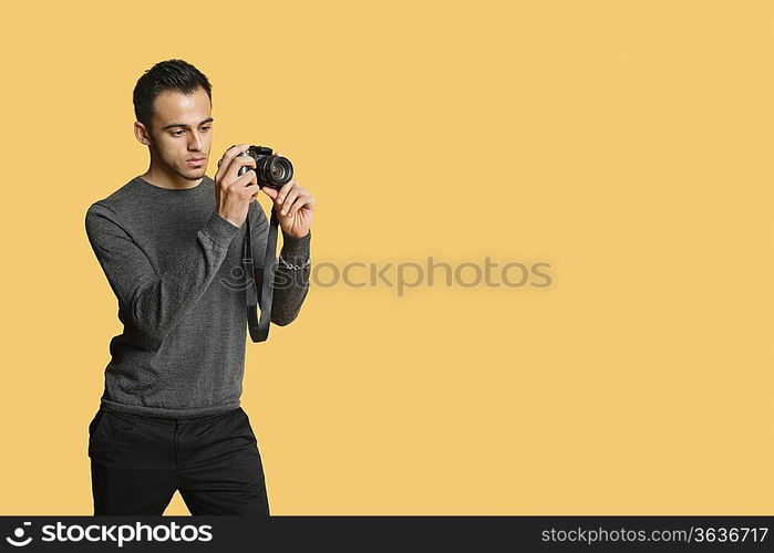 confident young man with digital camera over colored background