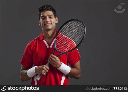 Confident young man with tennis racket over black background