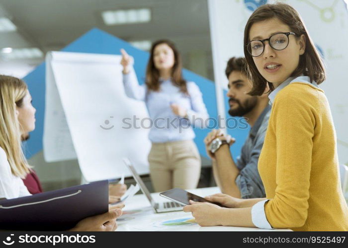 Confident young team leader giving a presentation to a group of young colleagues as they sit grouped by the flip chart in the small startup office