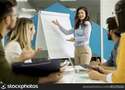 Confident young team leader giving a presentation to a group of young colleagues as they sit grouped by the flip chart in the small startup office