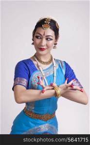 Confident young woman performing classical dance on gray background
