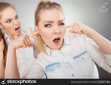 Conflict, bad relationships, friendship difficulties. Two young women having argument. Angry fury girl screaming at her friend or younger sister, female closing his ears, not listening. Fury girl screaming at her friend, female closing his ears
