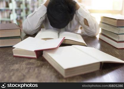confused and upset man with textbook stack on wooden desk in library