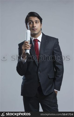 Confused businessman holding newspaper against gray background