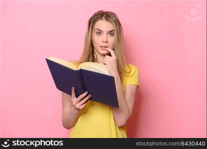 Confused cute girl thinking and reading the book isolated on colorful pink background