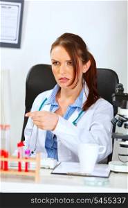 Confused doctor woman sitting at table and pointing finger in monitor&#xA;