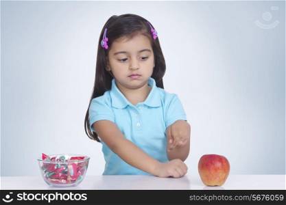Confused girl choosing between apple and sweet food against blue background