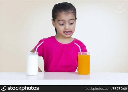 Confused girl choosing between juice and milk against colored background