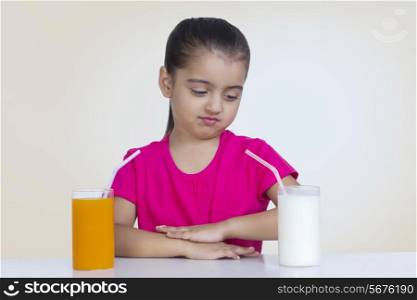 Confused girl choosing between orange juice and milk against colored background