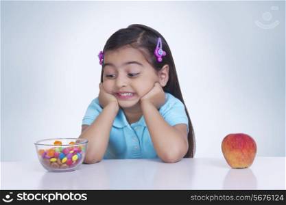 Confused girl choosing between sweet food and apple against blue background