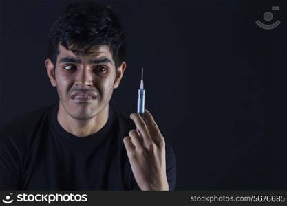 Confused male drug addict looking at syringe against black background