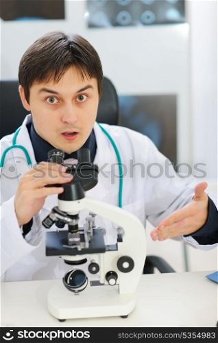 Confused male researcher pointing on microscope
