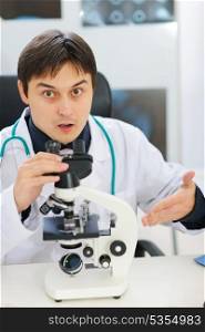 Confused male researcher pointing on microscope