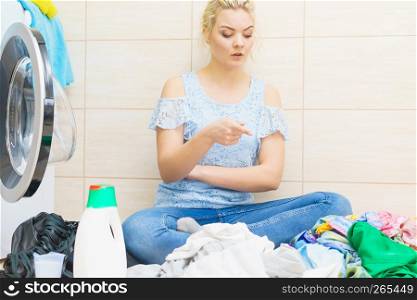 Confused woman having a lot of laundry to make. Unhappy female surrounded by big clothing piles stack sitting next to washing machine being tired houseworking.. Unhappy woman having a lot of laundry