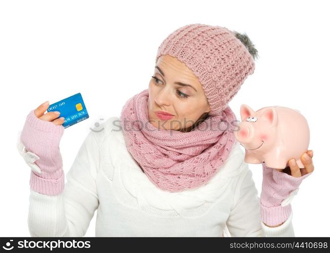 Confused woman in knit winter clothing holding credit card and piggy bank