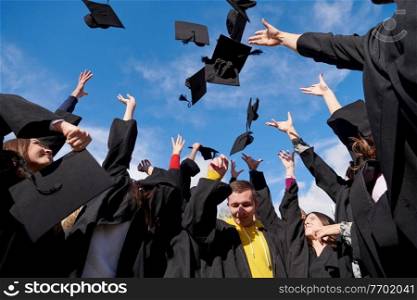 Congratulations  Low angle view of happy group of six young cheerful graduates in black gowns, throwing up their head wear in the air and celebrating, in blue summer sky, laughing, enjoying