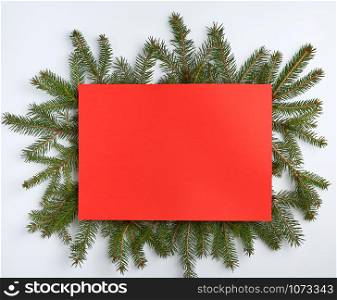 congratulatory Christmas background with an empty red sheet and green branches of spruce on a white background, mock up