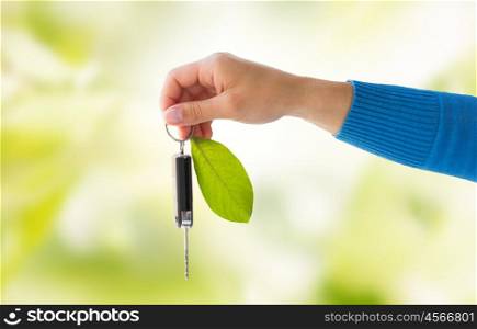 conservation, environment, people, transport and ecology concept - close up of hand holding car key with green leaf trinket over green natural background