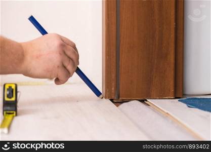 Construcion worker measuring floor panels using ruler and pencil. Home renovation concept.. Man measuring floor panels