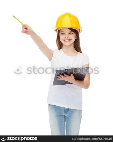 construction and people concept - smiling little girl in protective helmet with clipboard pointing finger at something