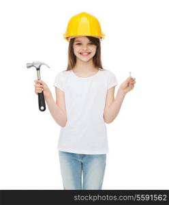 construction and people concept - smiling little girl in protective helmet with hammer and big nail