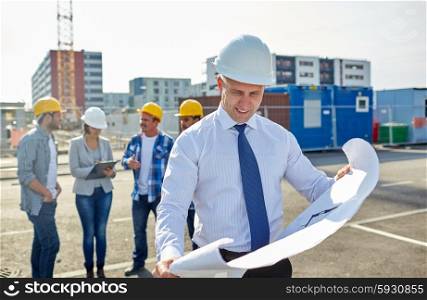 construction, architecture, business, teamwork and people concept - male architect with blueprint over group of builders on construction site