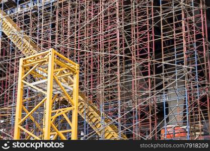 Construction background showing scaffolding on a construction site with a yellow trash chute running diagonally through the complexity.